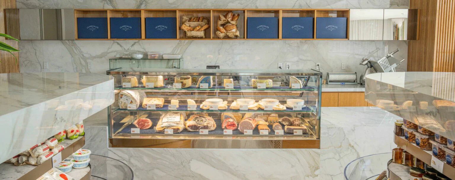 meats and cheeses displayed in a case with breads in baskets.