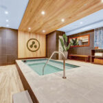 Inside of a spa area with an inground hot tub adjacent to showers with a beautiful wood bench and shelving.