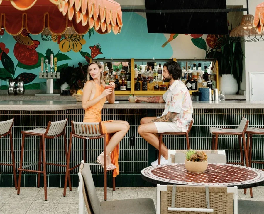 a couple sitting at an outside bar lounge area drinking drinks.