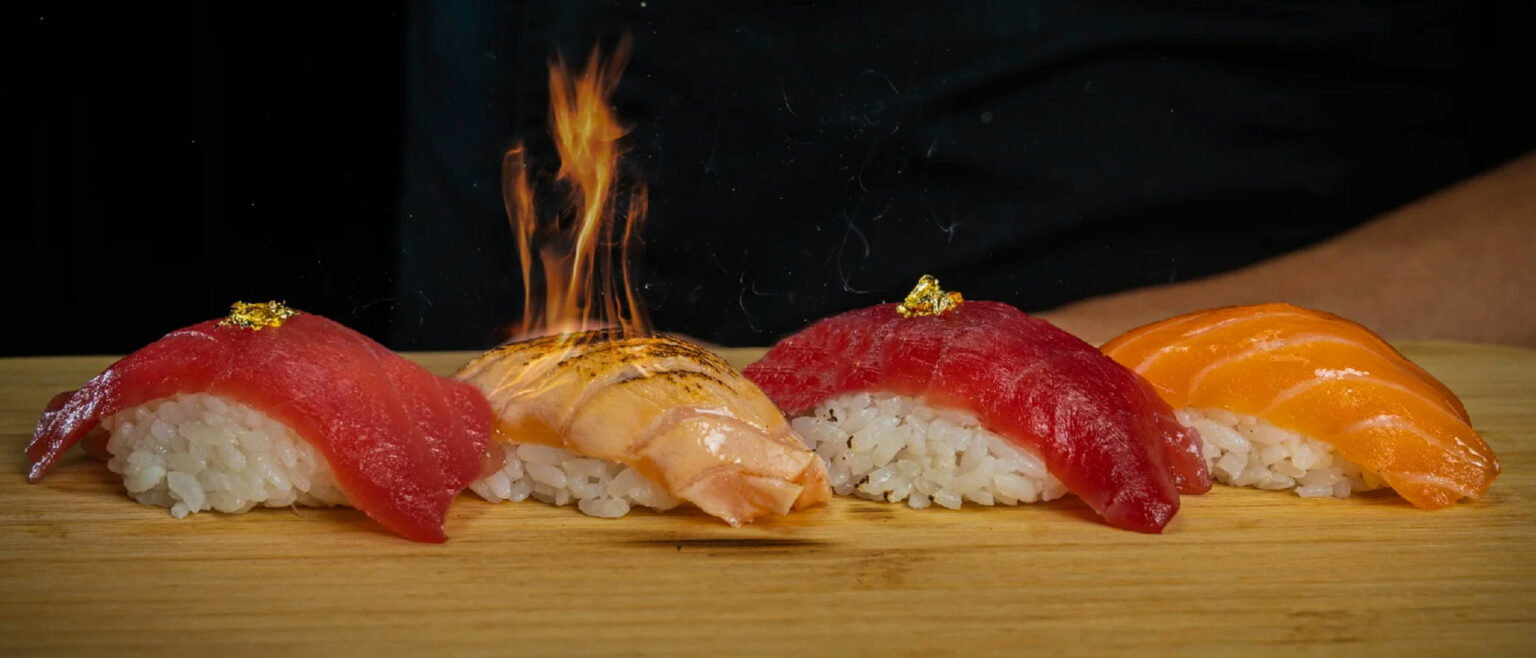 Sushi pieces on a wooden board topped with edible gold flakes and flames.