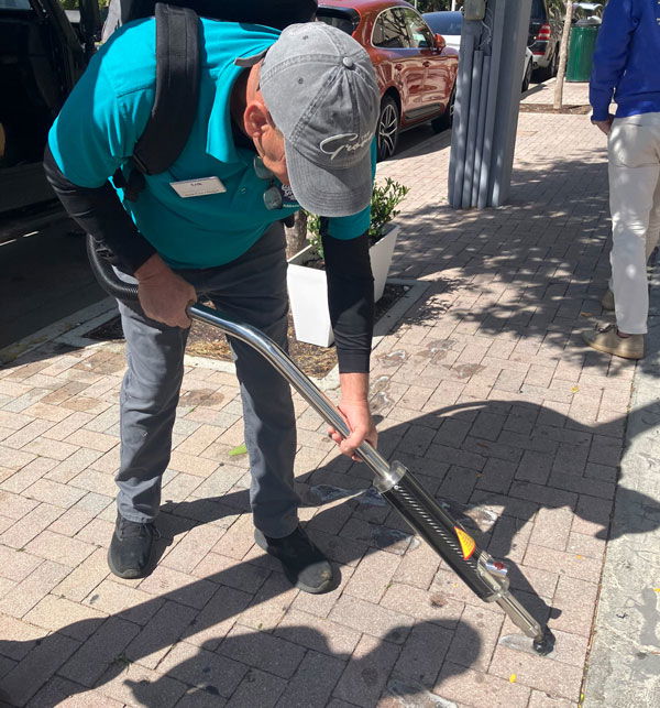 Man in teal shirt using vacuum machine to remove gum from pavement