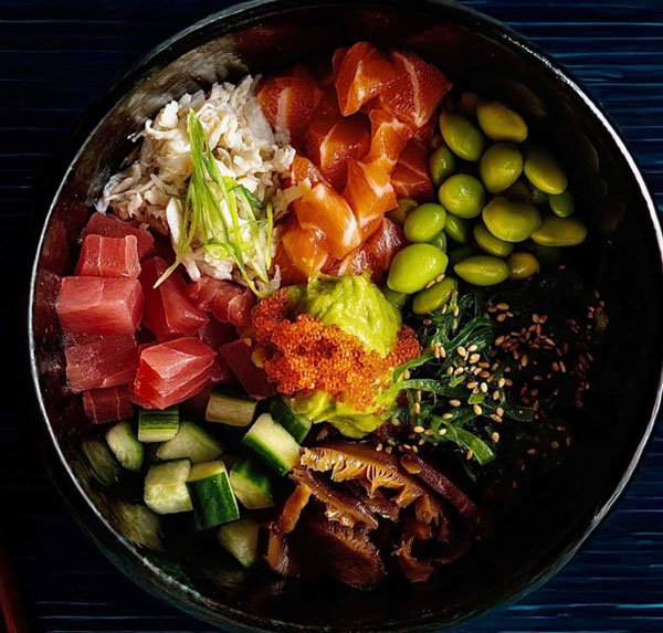 mixed bowl of fresh sushi salmon and other items such as seaweed salad, cucumber, rice, edamame.