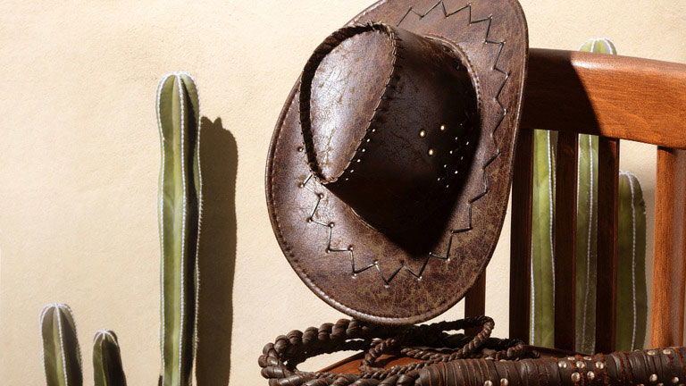 a cowboy western hat on a wooden chair, with a lasso and a cactus next to the chair.