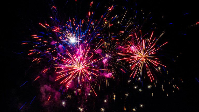 Fireworks, red, orange and blue light up the dark night sky.