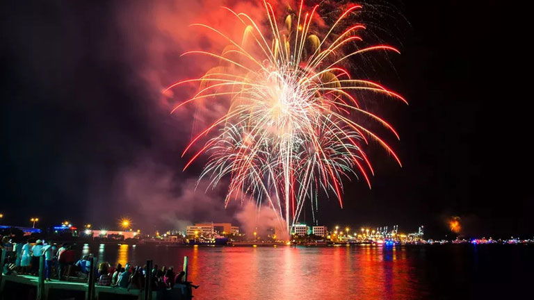 Fireworks, red, orange and blue light up the dark night sky and water.