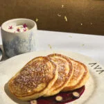 Fluffy pancakes with berry sauce next to a latte topped with edible flowers.
