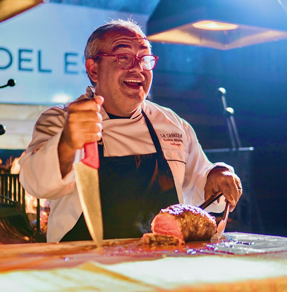 Chef wearing glasses with a knife and tongs cutting up a steak