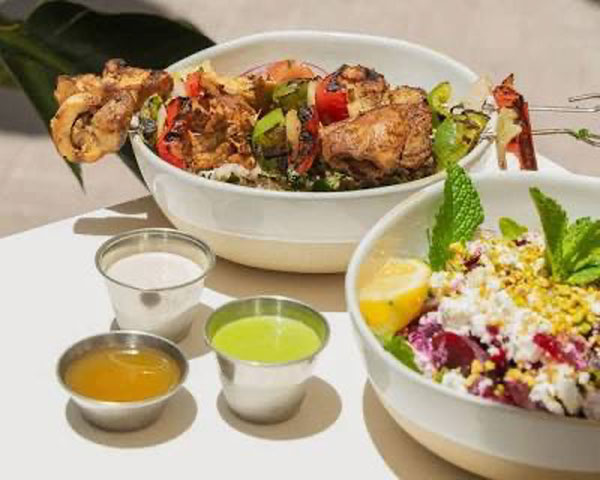 Chicken kabob with vegetables with a bowl of rice and a variety of side of sauces.