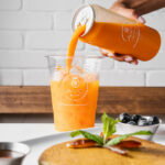 Avo Miami juice being poured into a cup of ice next to plates of breakfast dishes.