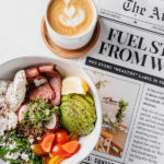 Healthy meal topped with tomatoes, avocado served with a latte and newspaper
