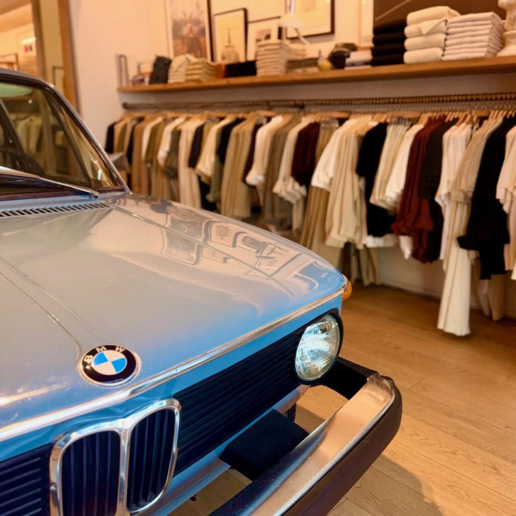 vintage BMW car inside of a store display next to clothes on hangers and shelves.