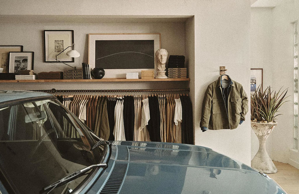 variety of different clothing items, books and artwork on display at a clothing store, next to a car.