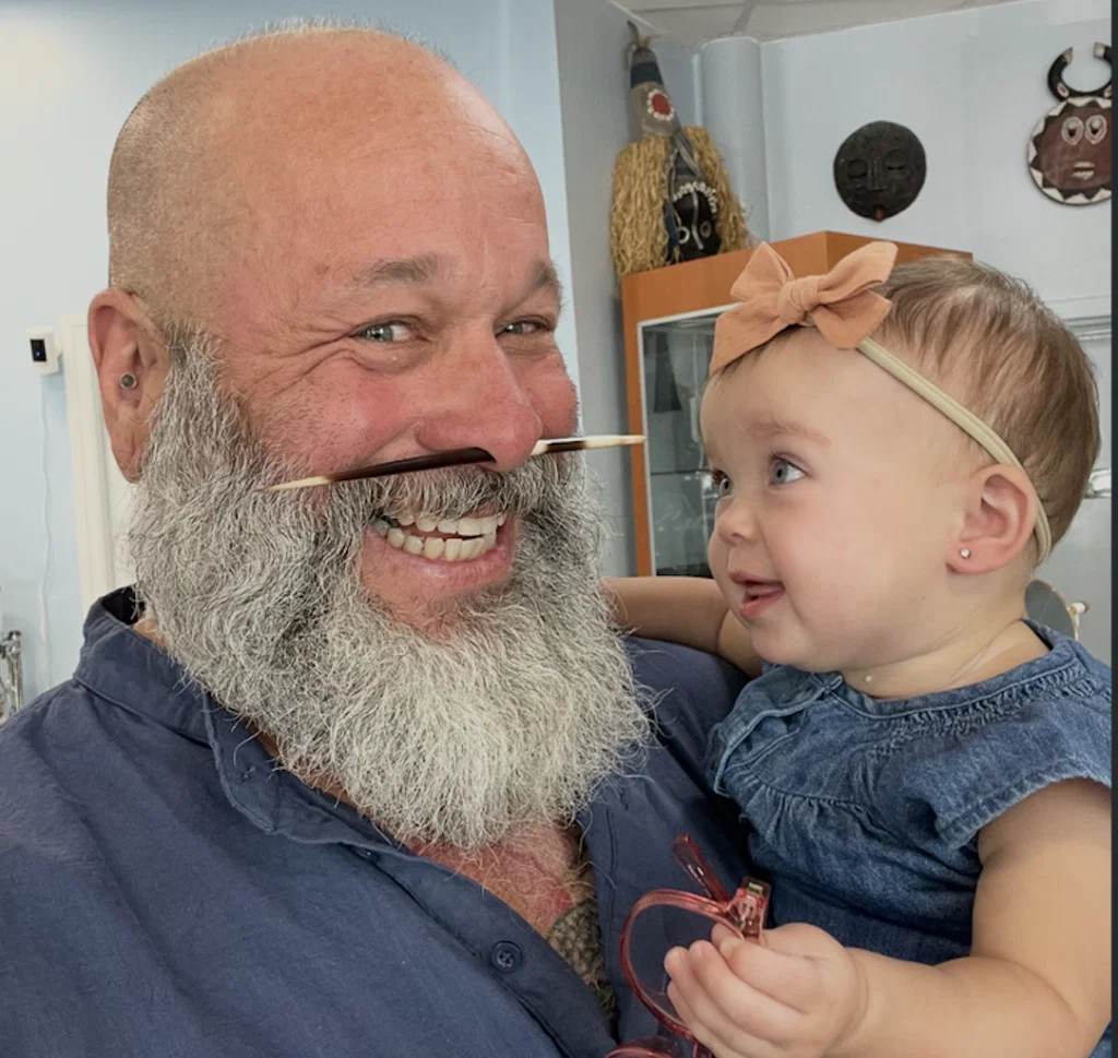 smiling baby with pierced ears being held by a bearded man with a nose piercing