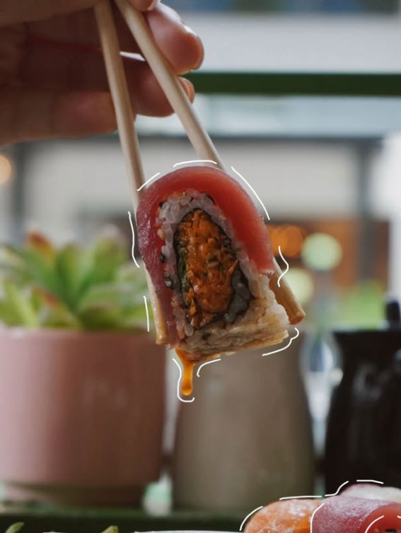 a person holding a pair of chopsticks picking up a piece of sushi with squiggle drawing illustration lines around the food.