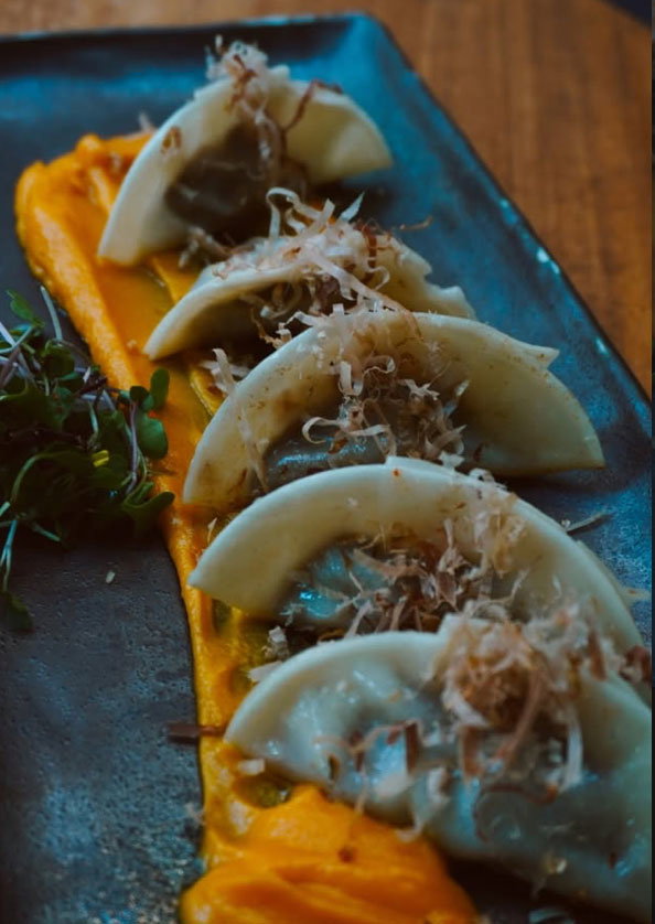 Steamed dumplings plated on top of a plate with orange puree and topped with shredded coconut.