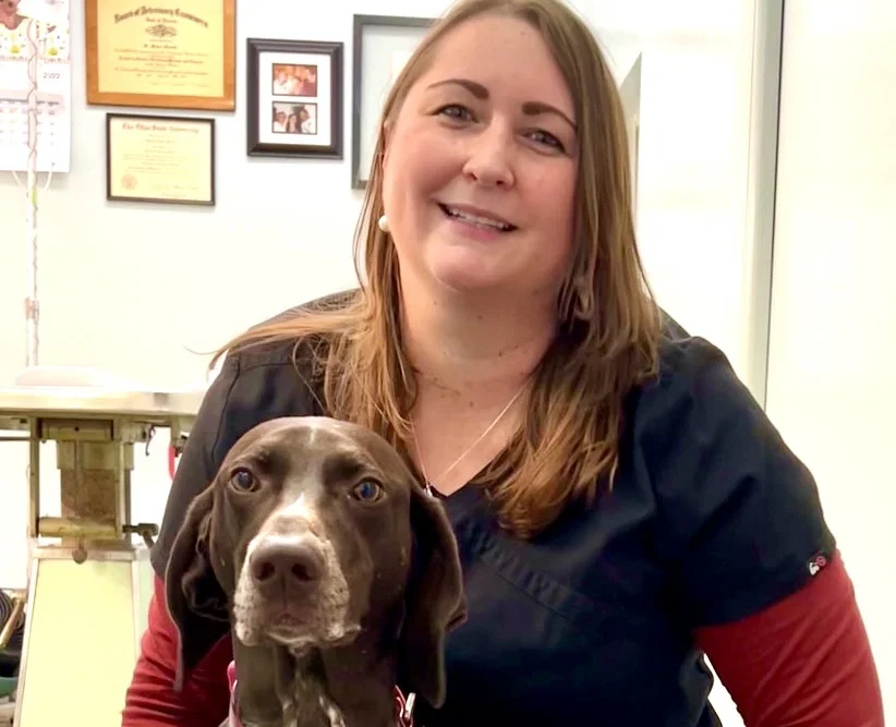 Vet, smiling wearing scrubs posing with a dog