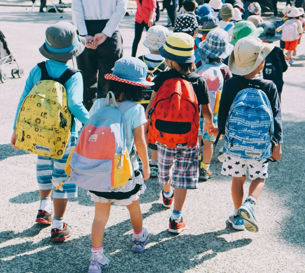 children wearing backpacks and sunhat walking