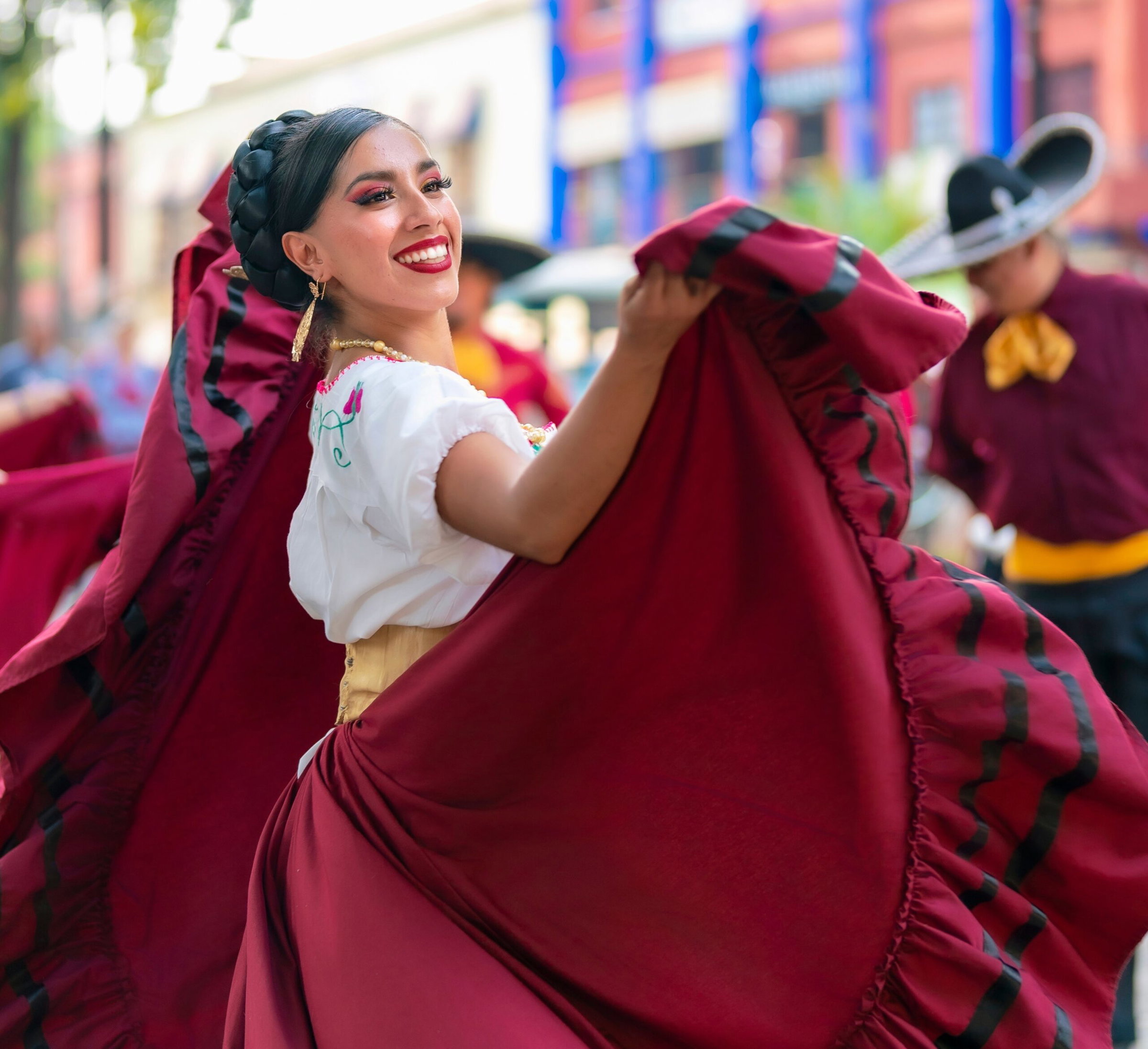 Latina woman in a vibrant traditional dress twirling joyfully during a performance.