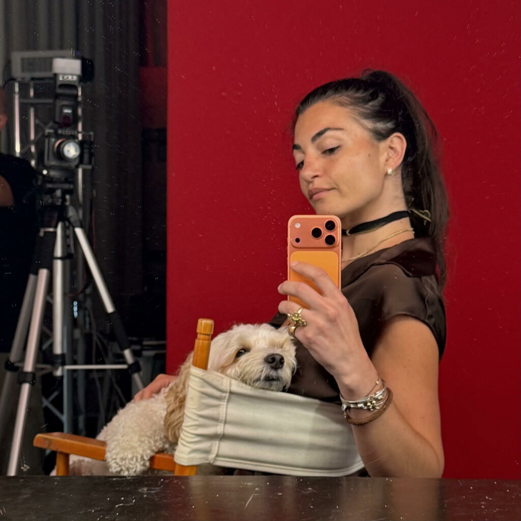 Lady taking a selfie while sitting in a director’s chair with her small dog.