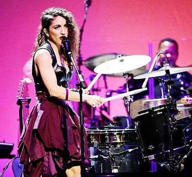A young lady playing drums and singing into a microphone.